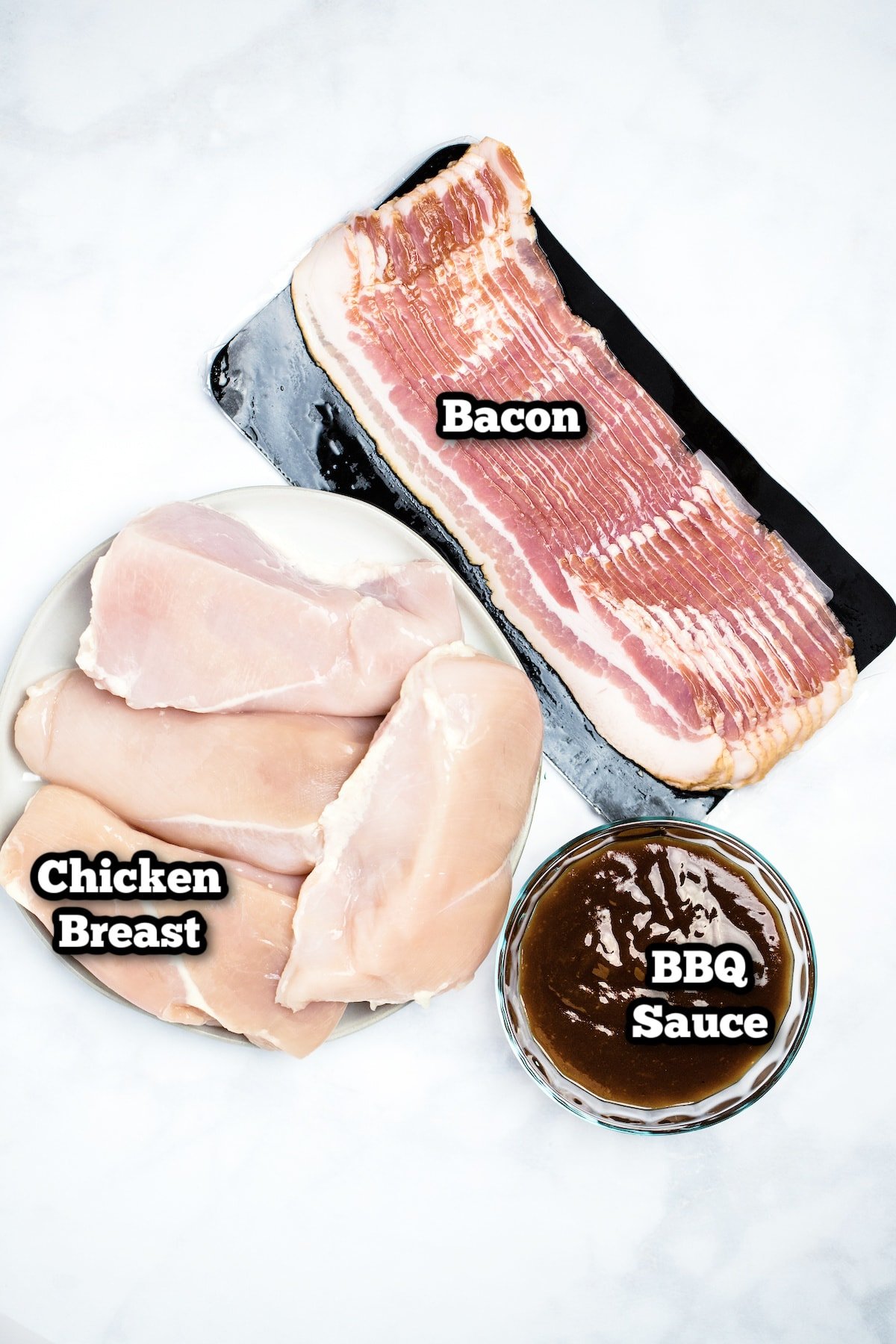 Individual ingredients for bbq bacon wrapped chicken breasts on a marble table.