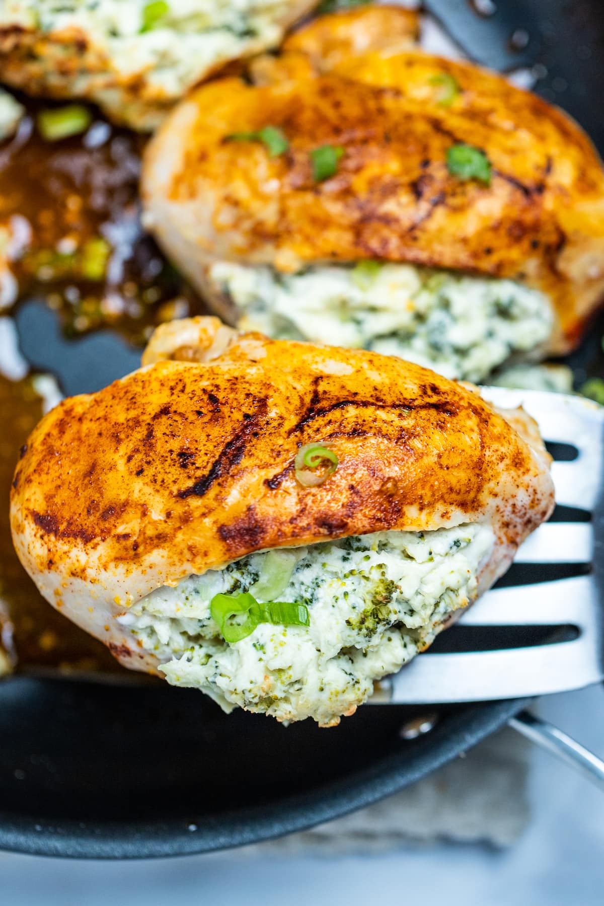 A spatula lifting a piece of broccoli and cheese stuffed chicken out of a skillet.