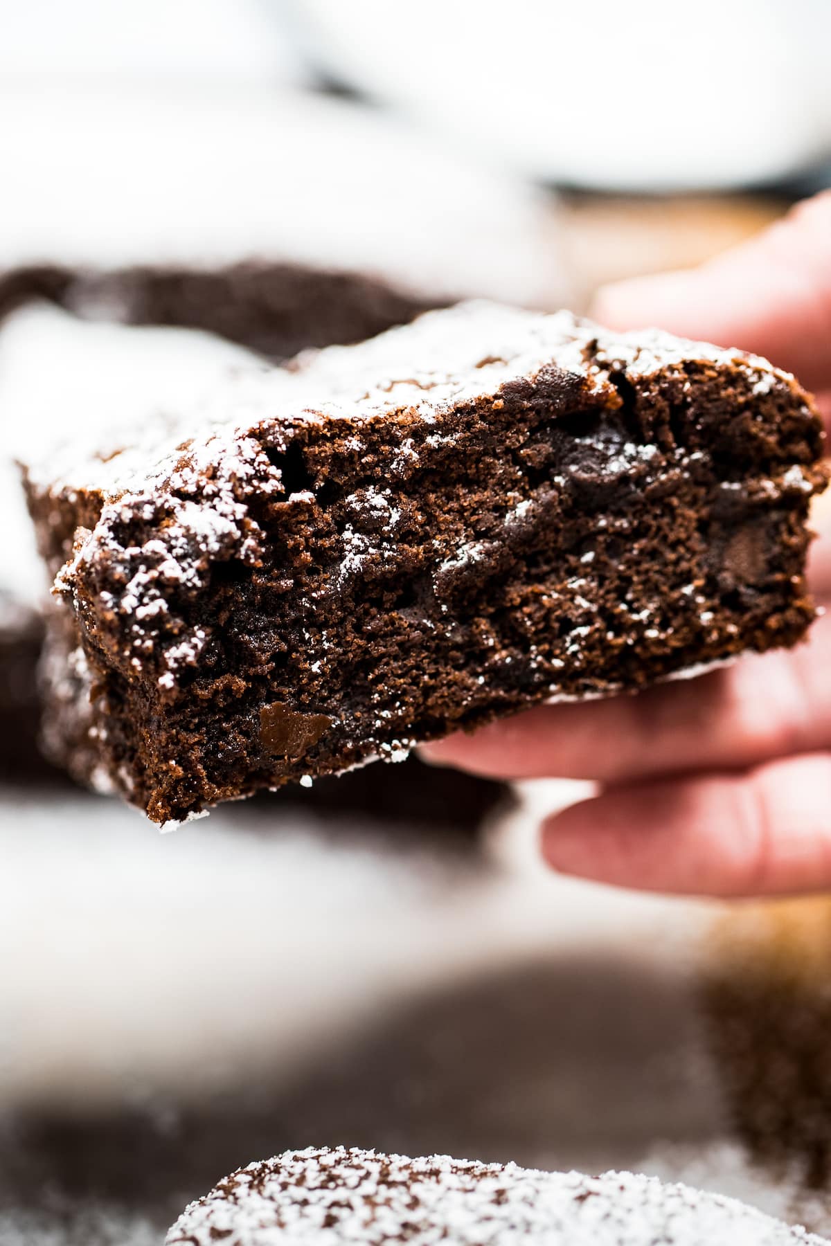 A hand holding a fudgy gluten free brownie with the chocolate edge showing.
