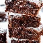 Four gluten free brownies stacked on top of each other dusted with powdered sugar.