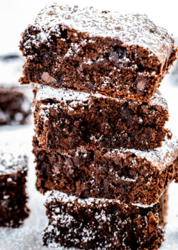 Four gluten free brownies stacked on top of each other dusted with powdered sugar.