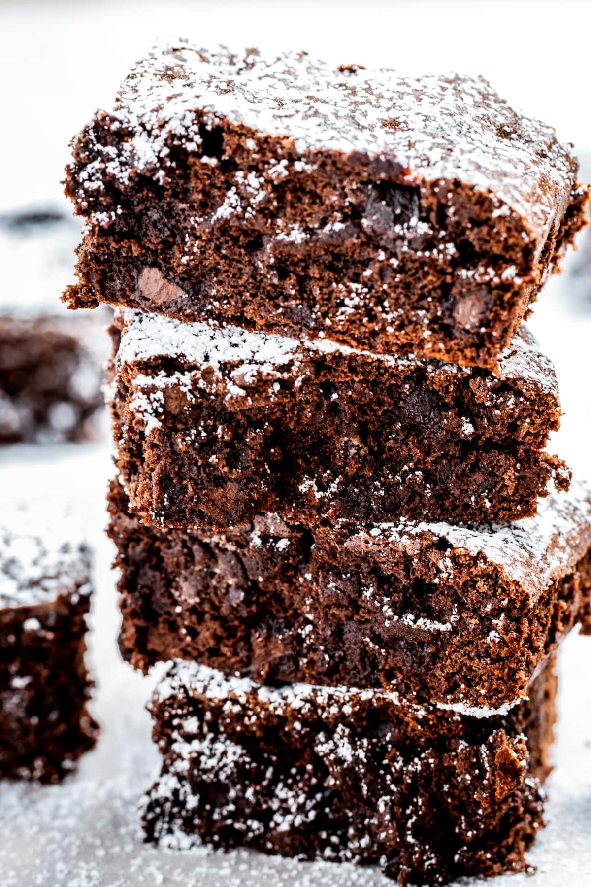 Four gluten free brownies stacked on top of each other dusted with powdered sugar.