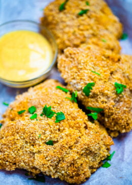 Three pieces of crispy oven fried chicken on parchment paper next to dipping sauce.