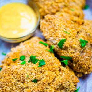 Three pieces of crispy oven fried chicken on parchment paper next to dipping sauce.