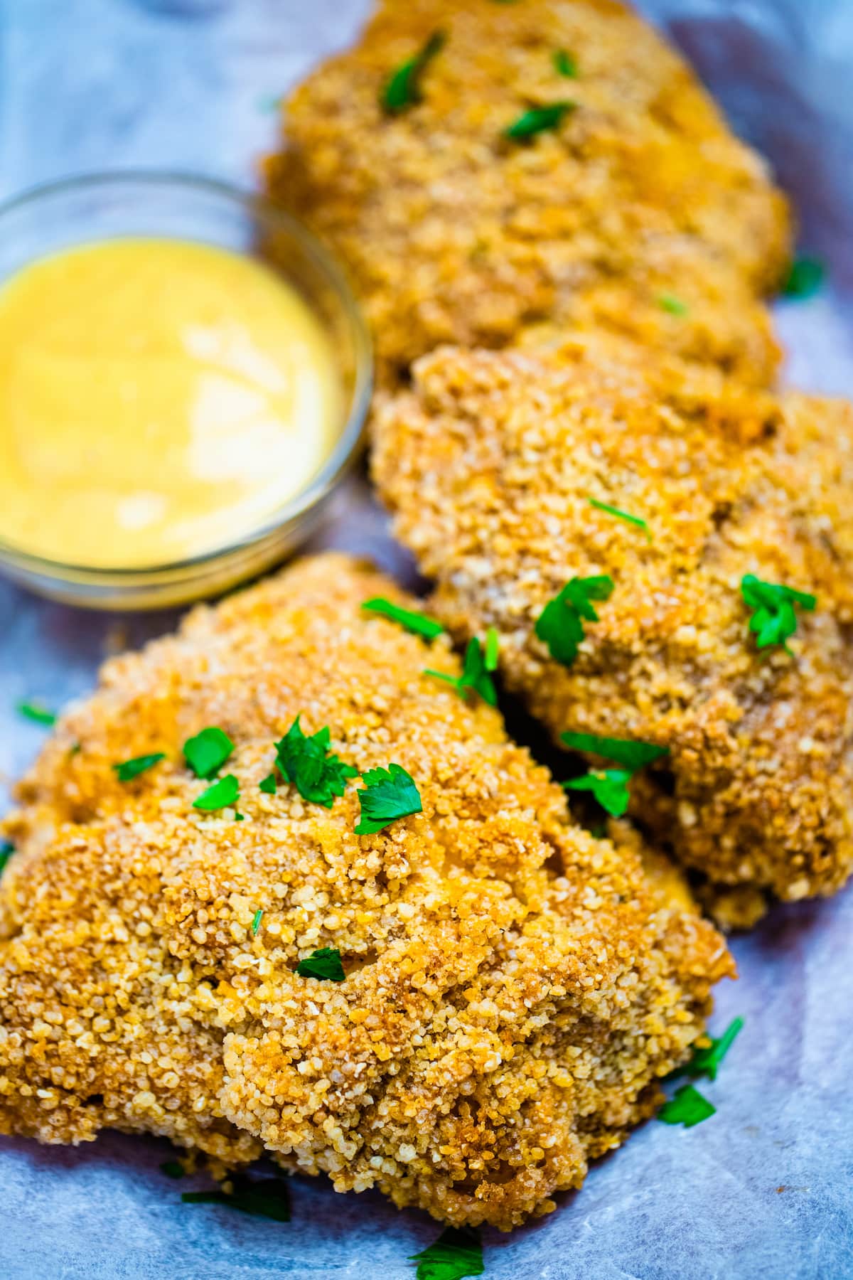 Three pieces of crispy oven fried chicken on parchment paper next to dipping sauce.