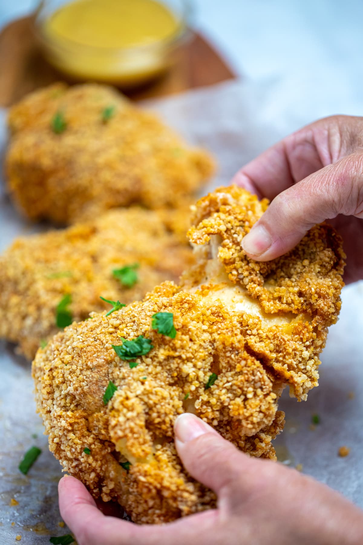 A piece of crispy chicken being pulled apart by two hands.