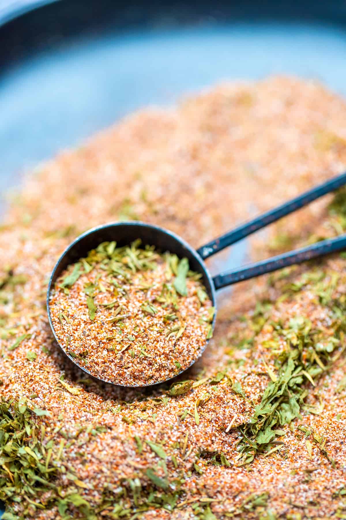 A tablespoon scooping up rotisserie chicken seasoning from a plate.