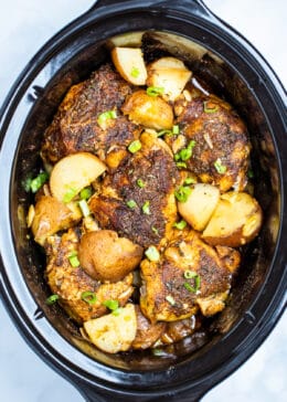 Slow cooker full of chicken thighs and potatoes topped with chopped green onions.