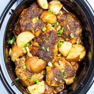 Slow cooker full of chicken thighs and potatoes topped with chopped green onions.