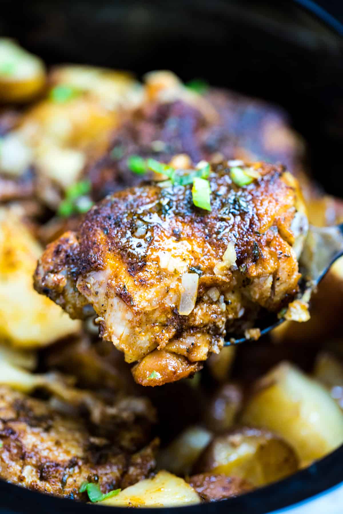 A spatula lifting a juicy chicken thigh out of the slow cooker.