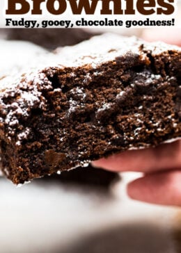 Pinterest pin with a photo of a hand holding a brownie with the chocolate fudgy side showing.