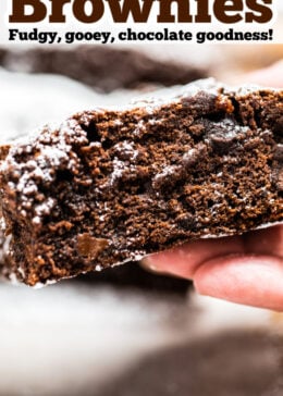 Pinterest pin with a photo of a hand holding a brownie with the chocolate fudgy side showing.