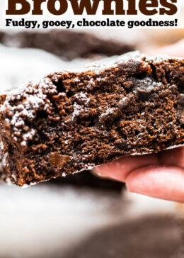 Pinterest pin with a photo of a hand holding a brownie with the chocolate fudgy side showing.