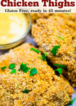 Pinterest pin of oven friend chicken thighs with a crispy piece of chicken on top of parchment paper next to dipping sauce.