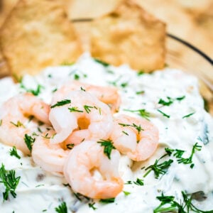A bowl of shrimp dip topped with chopped dill and mini shrimp next to crackers.