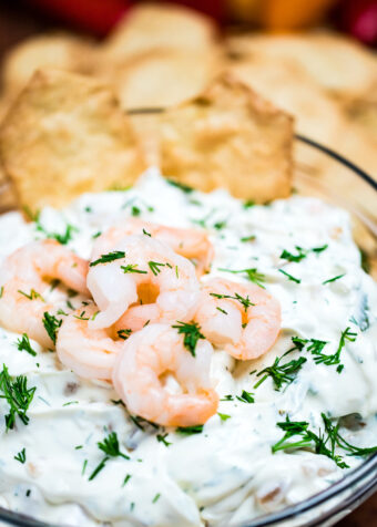 A bowl of shrimp dip topped with chopped dill and mini shrimp next to crackers.