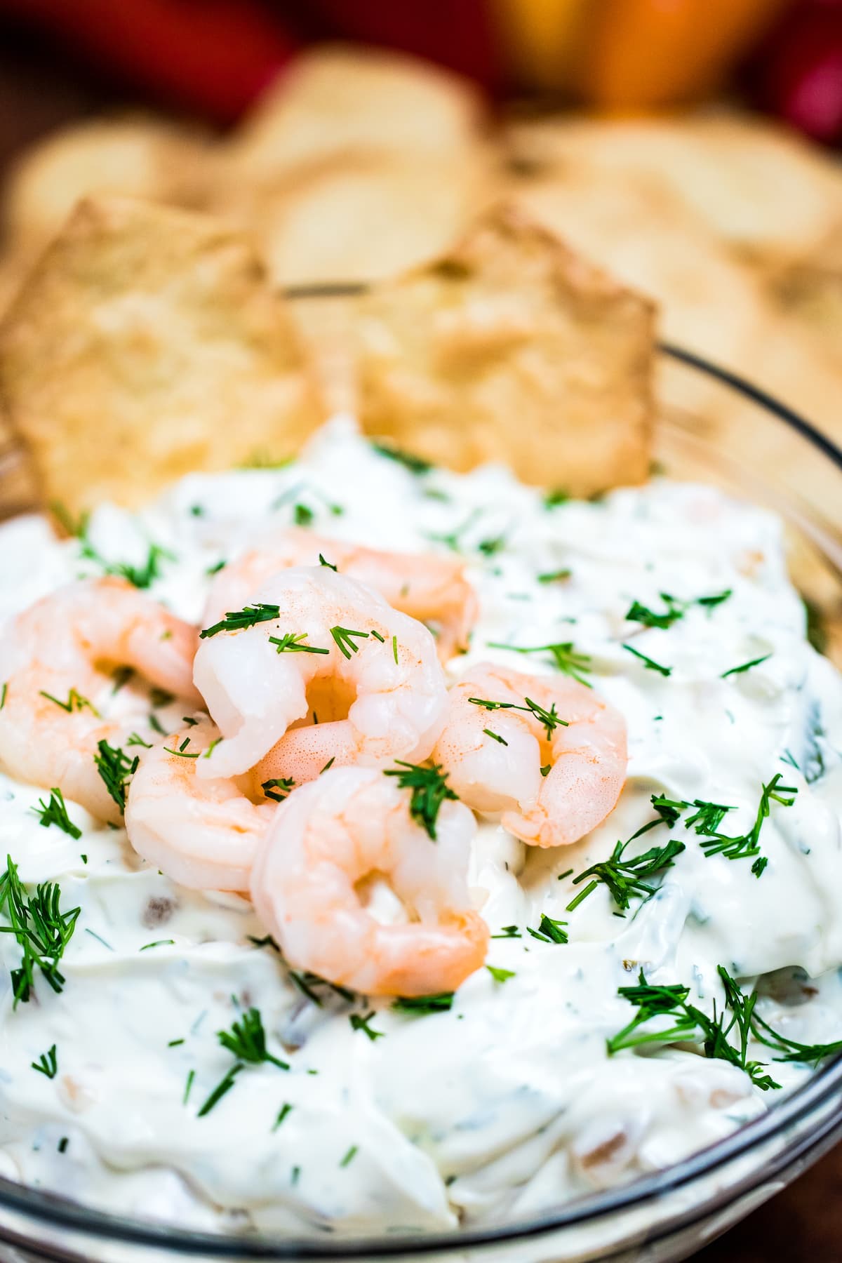 A bowl of shrimp dip topped with chopped dill and mini shrimp next to crackers.