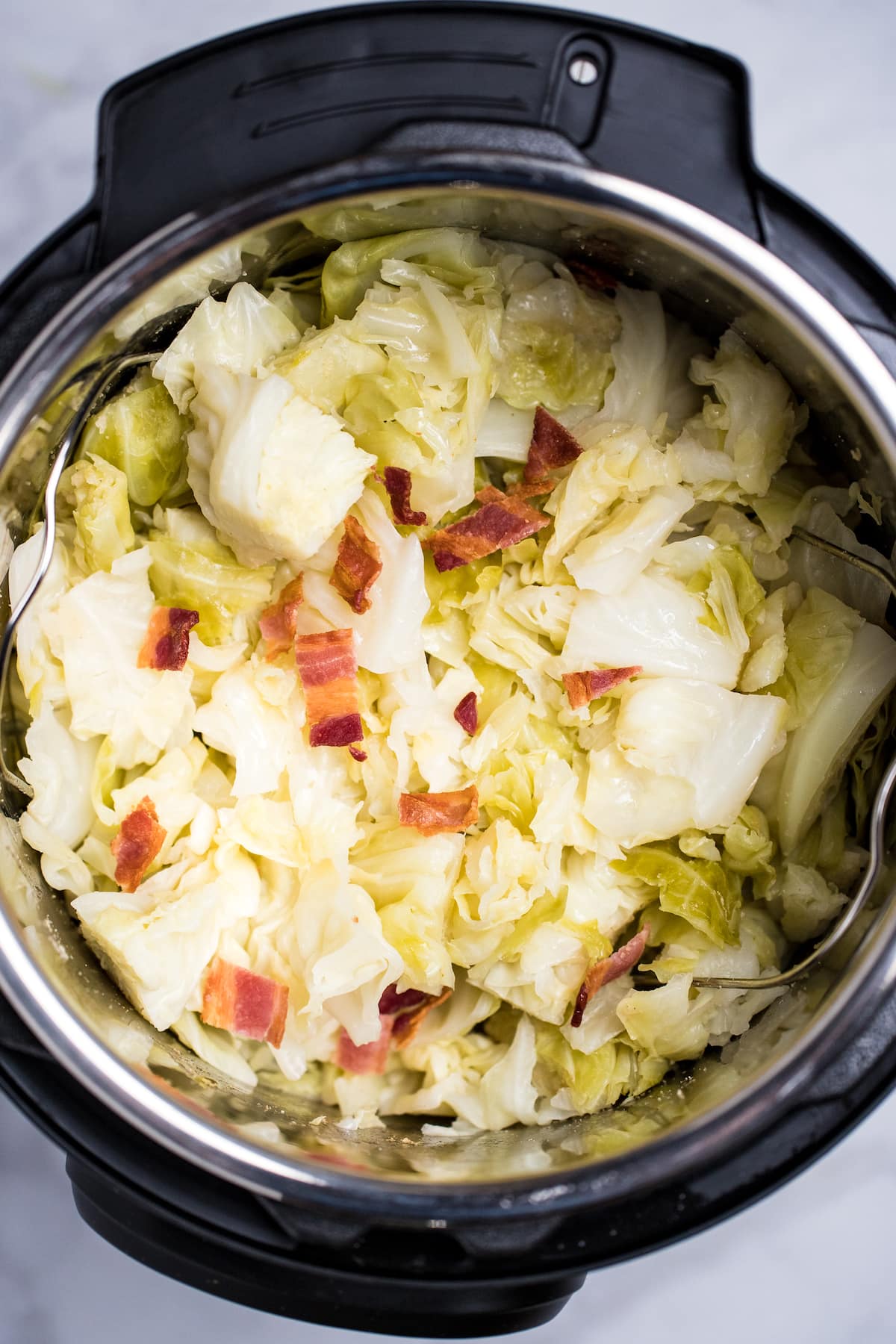 An instant pot full of cooked buttered cabbage topped with crispy bacon pieces.