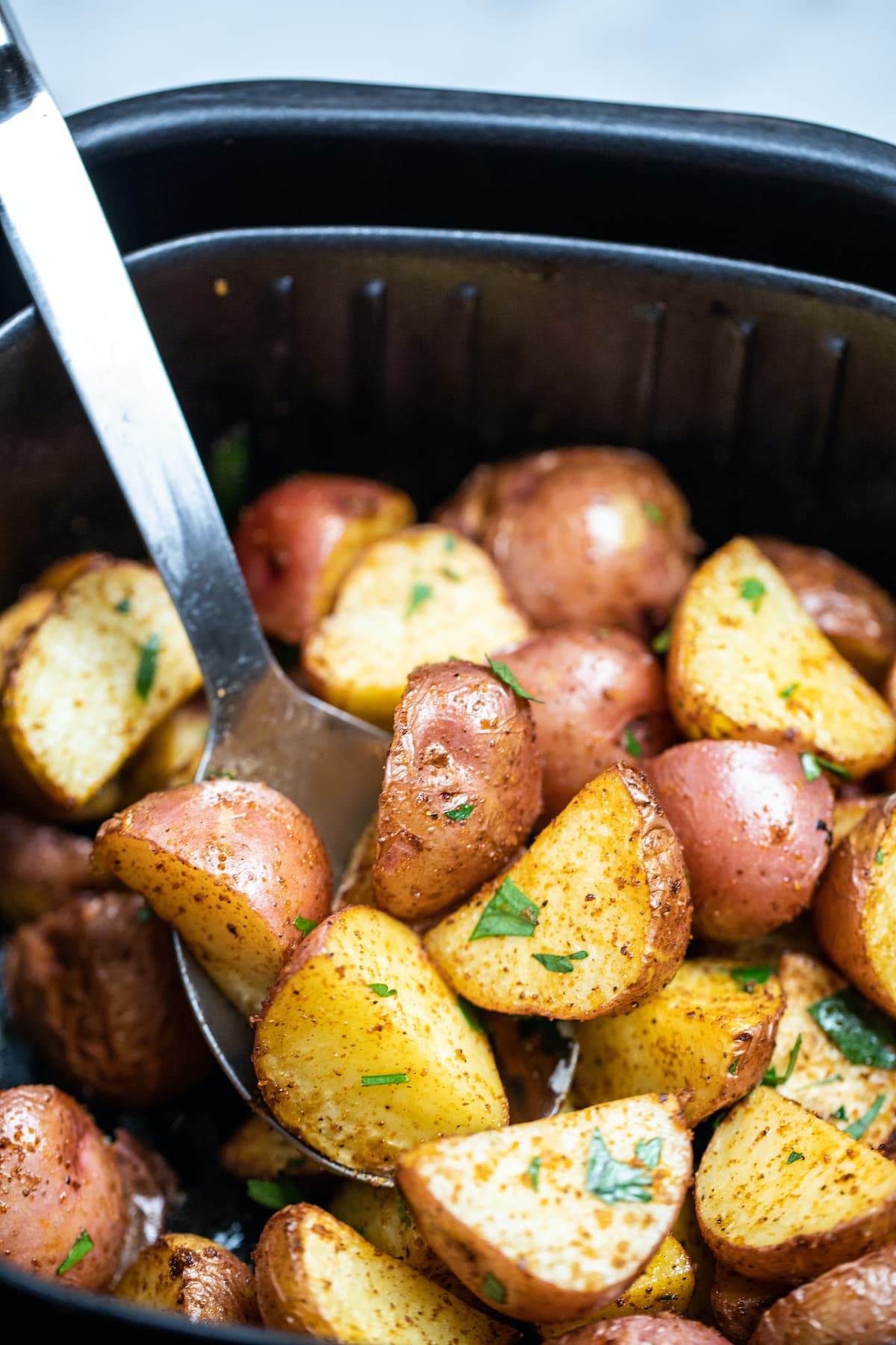 Red potatoes in an air fryer being lifted up by a spoon.