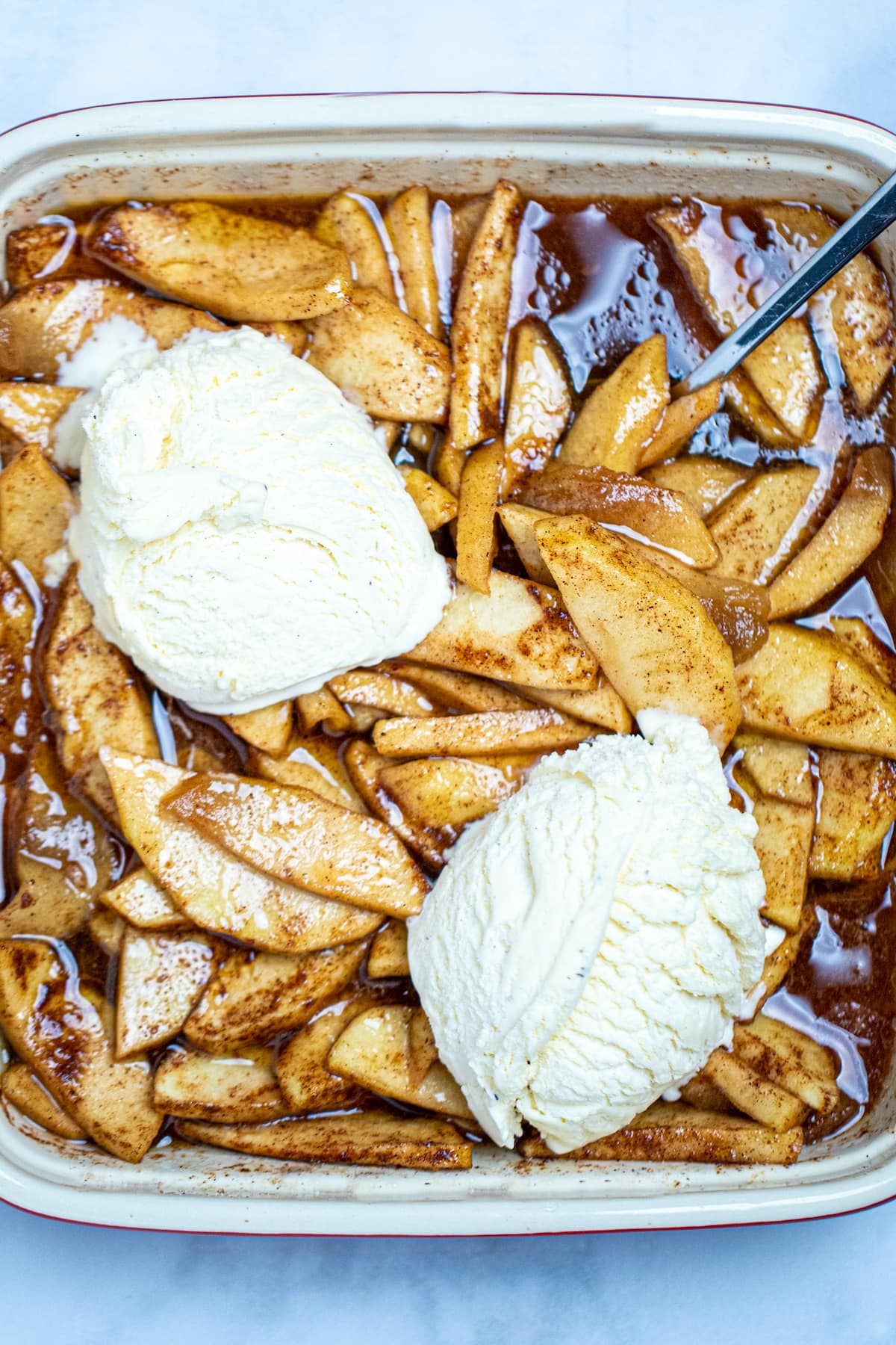 Photo of cinnamon baked apple slices topped with ice cream in a baking dish with a spoon.