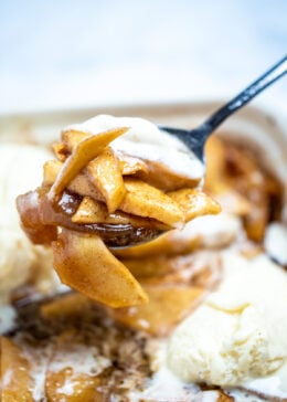 Photo of a spoon lifting cinnamon baked apple slices out of a baking dish.