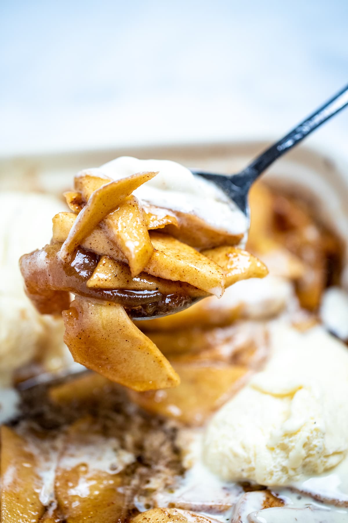 Photo of a spoon lifting cinnamon baked apple slices out of a baking dish.