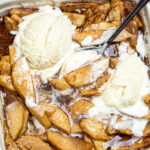 Photo of cinnamon baked apple slices topped with ice cream in a baking dish with a spoon.