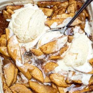 Photo of cinnamon baked apple slices topped with ice cream in a baking dish with a spoon.