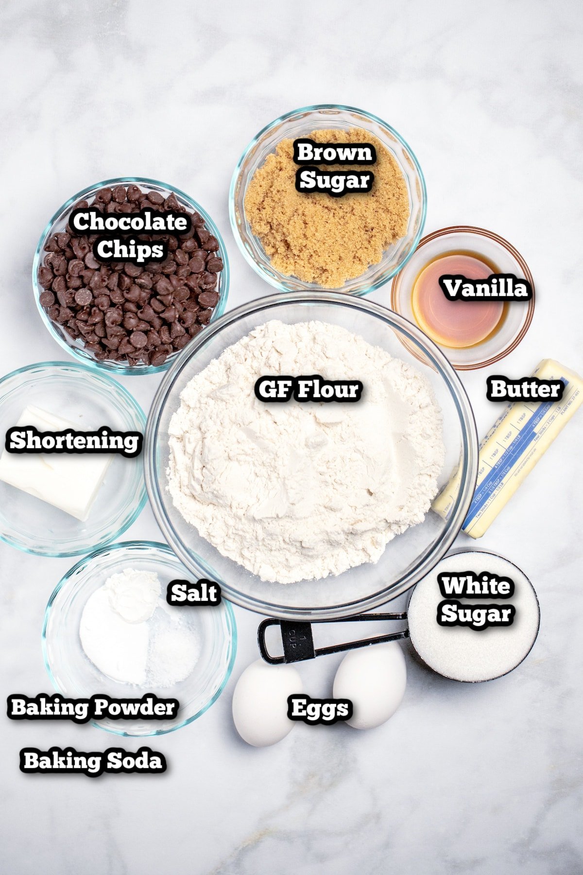 Individual ingredients for gluten free chocolate chip cookies on a marble table.
