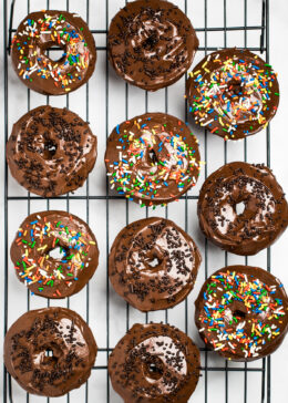 Cooling rack full of chocolate donuts with chocolate and rainbow sprinkles.
