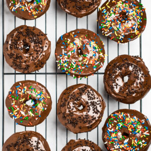 Cooling rack full of chocolate donuts with chocolate and rainbow sprinkles.