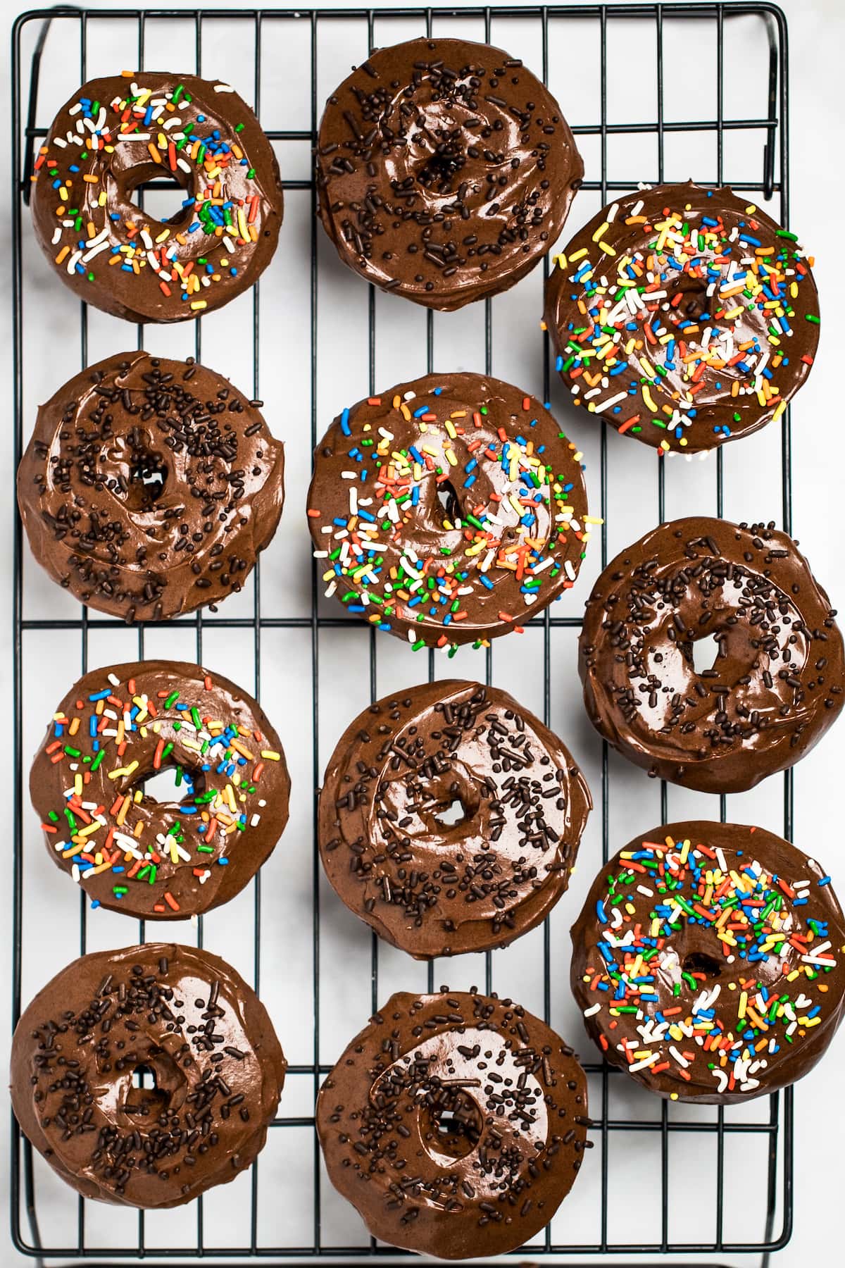 Cooling rack full of chocolate donuts with chocolate and rainbow sprinkles.