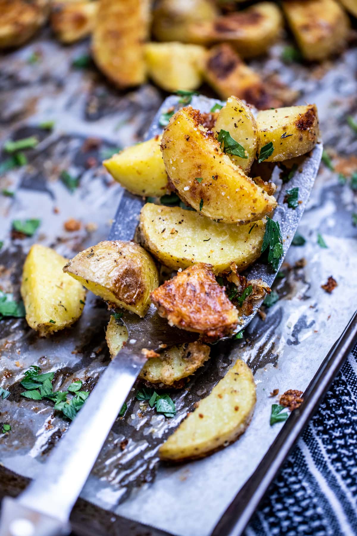 A sheet pan with a spatula lifting crispy roasted potatoes.