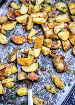 A sheet pan with a spatula lifting crispy roasted potatoes.