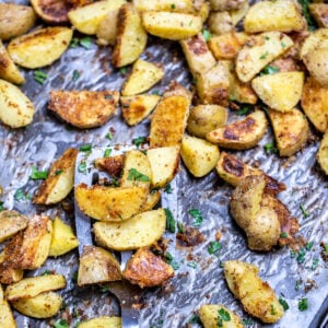 A sheet pan with a spatula lifting crispy roasted potatoes.