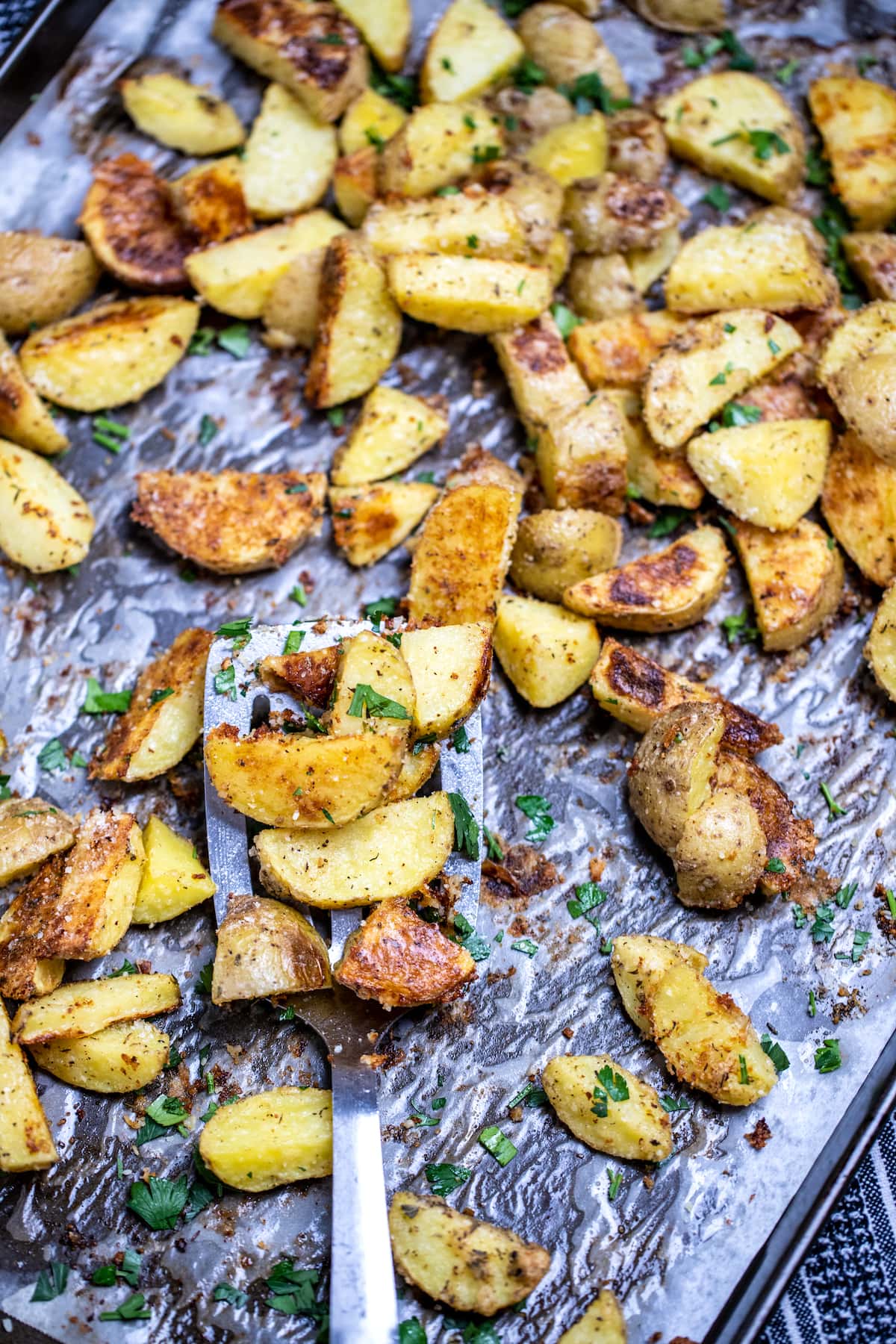 A sheet pan with a spatula lifting crispy roasted potatoes.