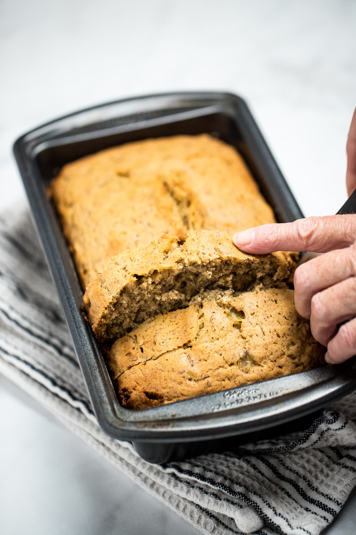 Pinterest pin with a loaf of banana bread in a bread pan on a table.