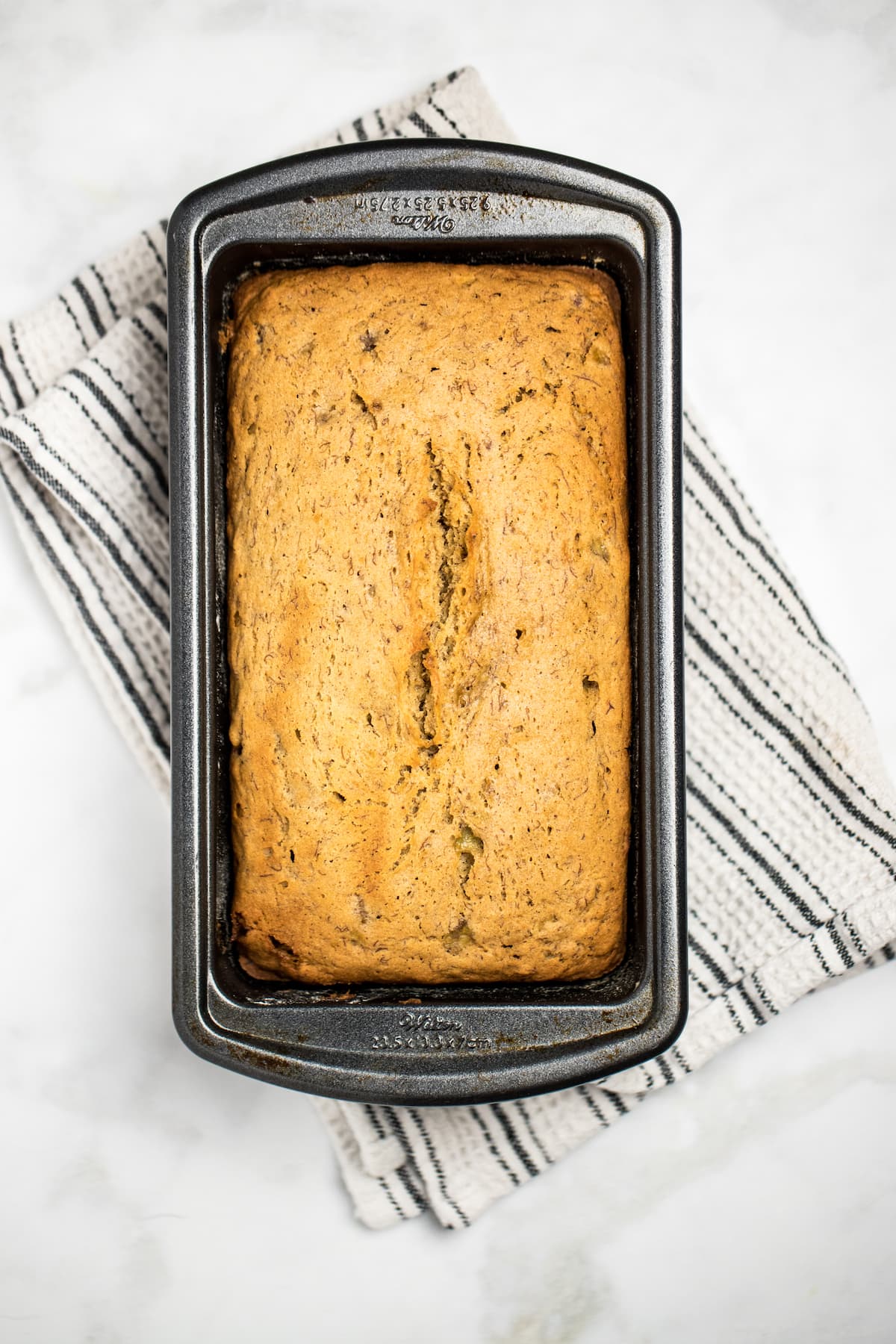 Pinterest pin with a loaf of banana bread in a bread pan on a table.