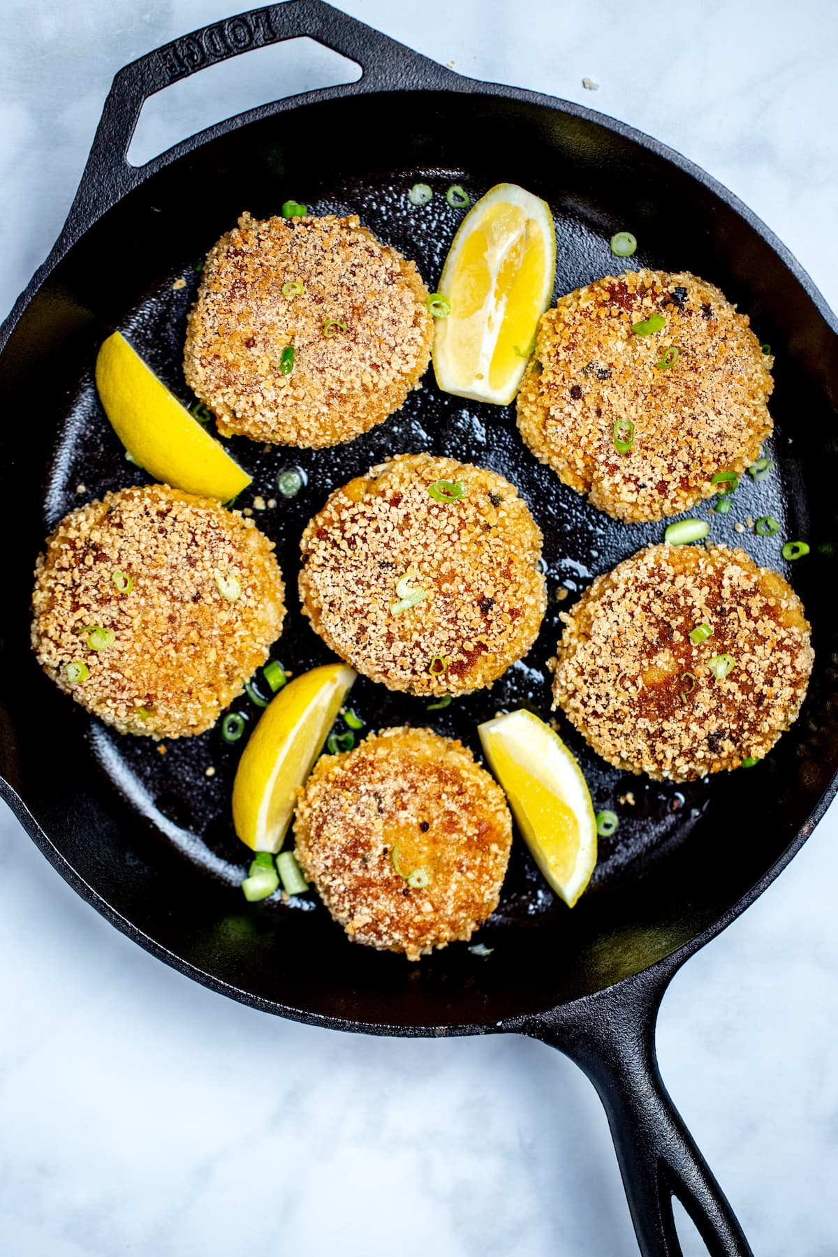 A skillet with gluten free crab cakes and lemon wedges.