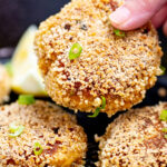 A hand holding a gluten free crab cake over a skillet.