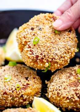 A hand holding a gluten free crab cake over a skillet.