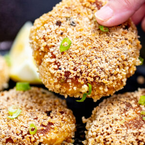 A hand holding a gluten free crab cake over a skillet.