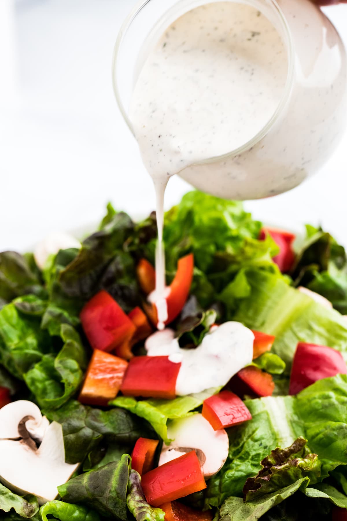 Small pitcher of buttermilk ranch dressing pouring onto a bowl of salad.