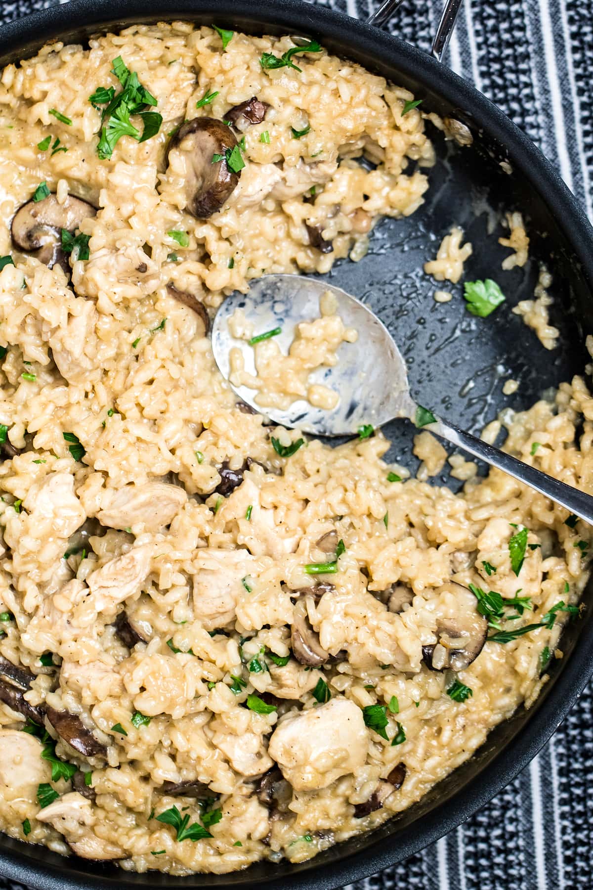 A skillet full of gluten free mushroom chicken risotto with a spoon.