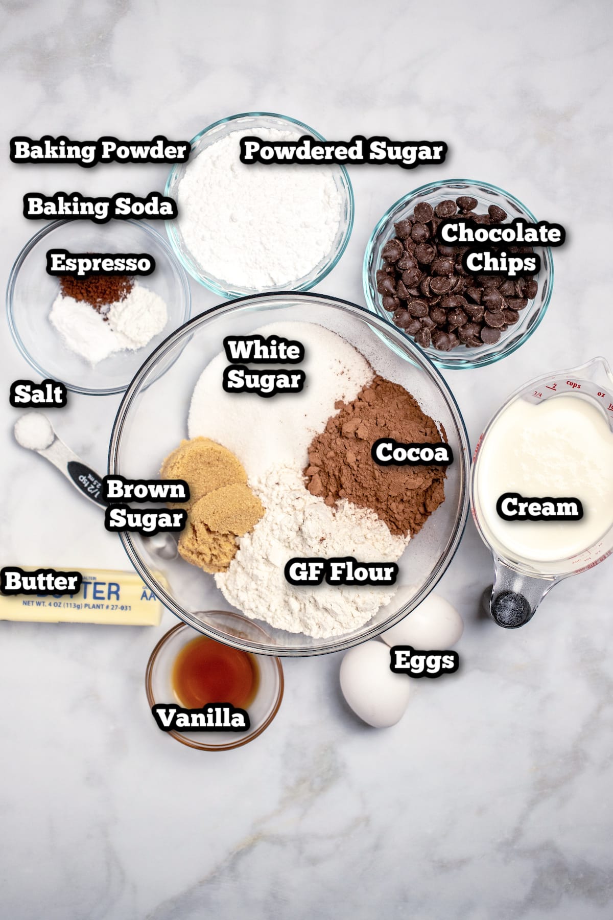 Individual ingredients for chocolate donuts on a marble table.