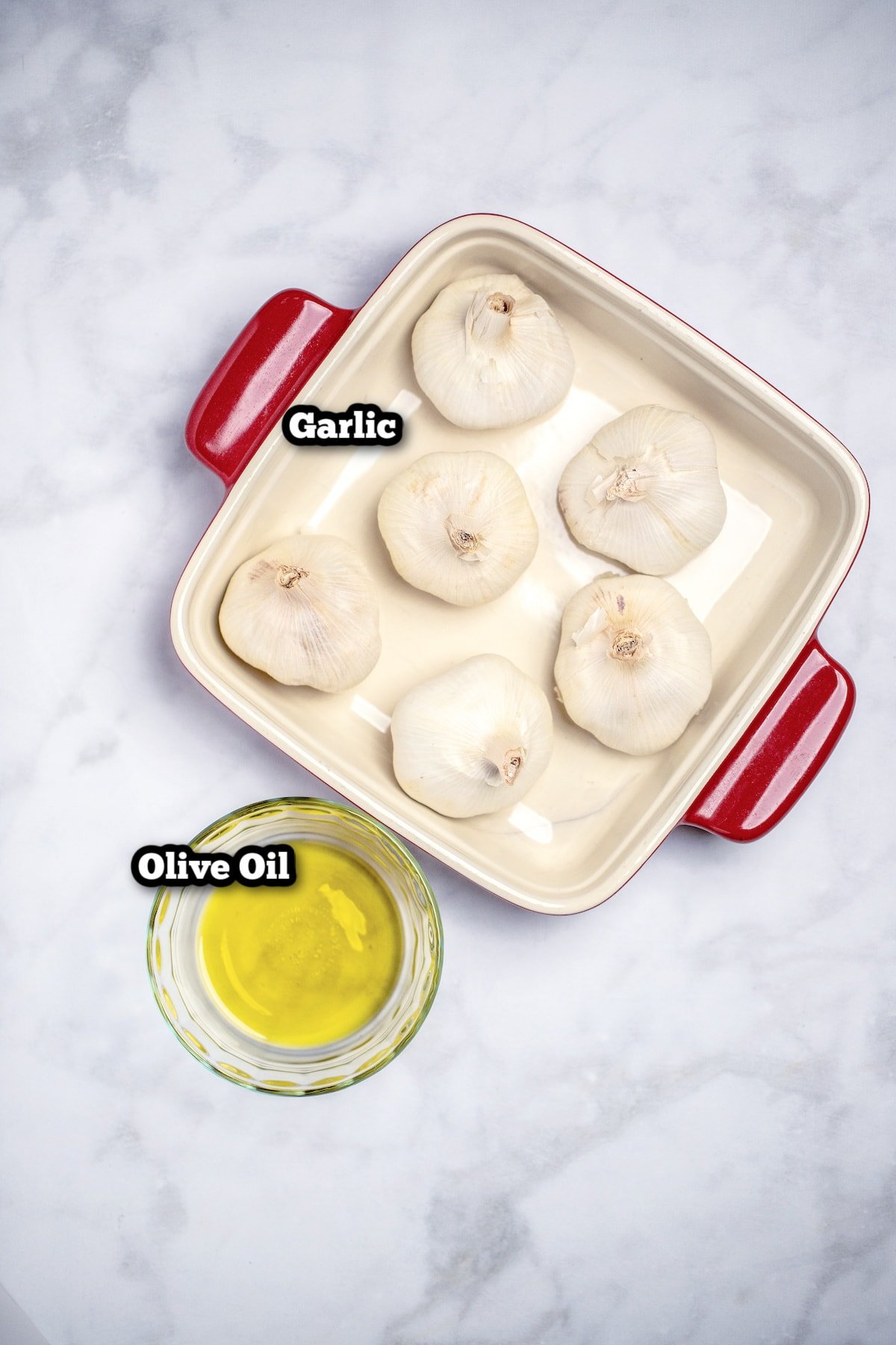 Individual ingredients for roasted garlic on a marble table.