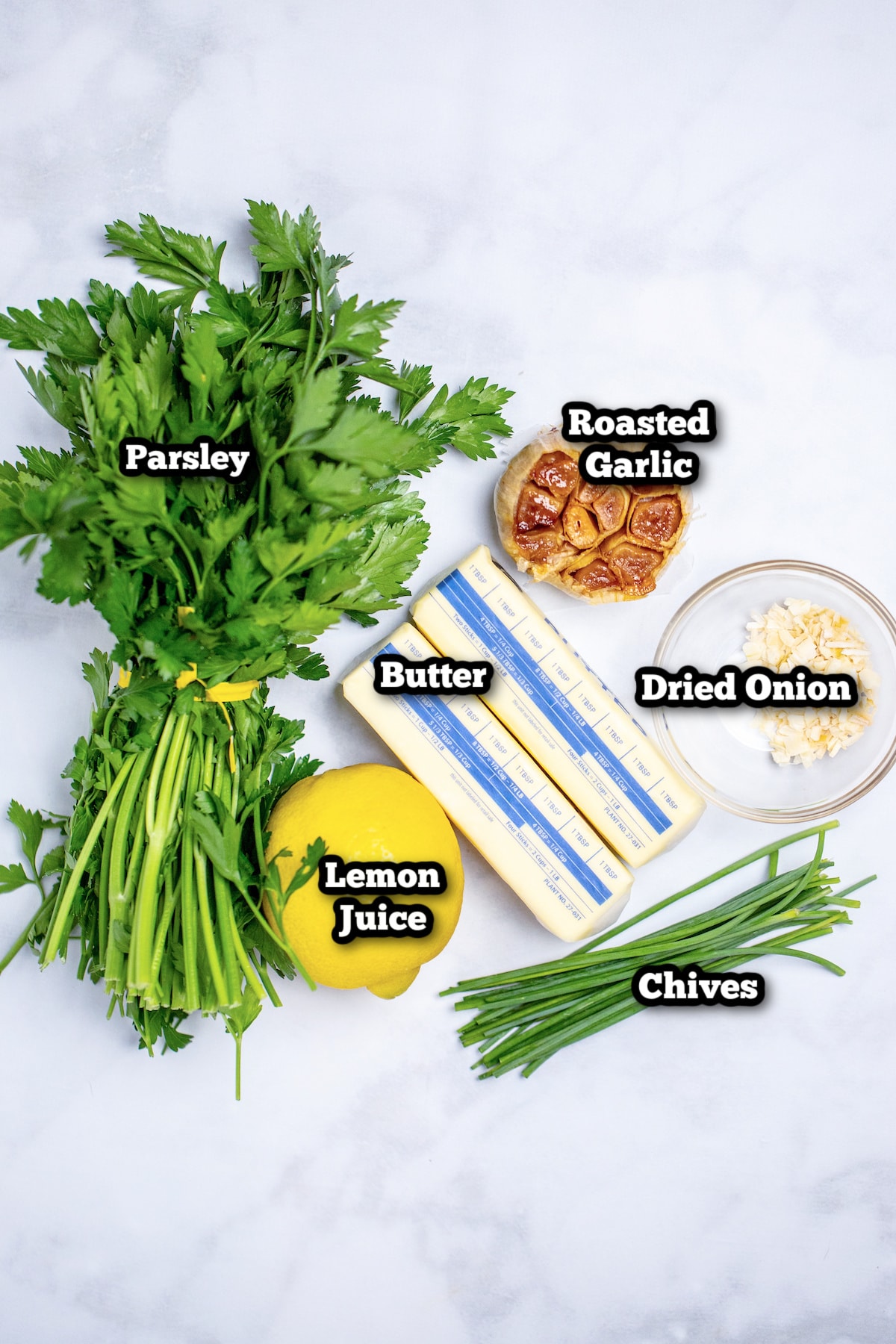 Individual ingredients for herb butter on a marble table.