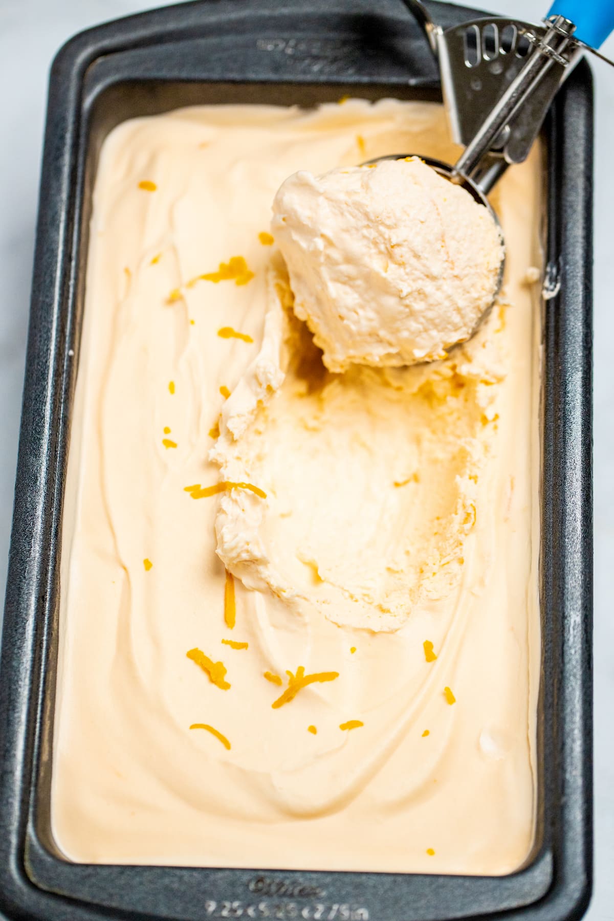 A bread pan full of orange ice cream with an ice cream scoop topped with orange zest.