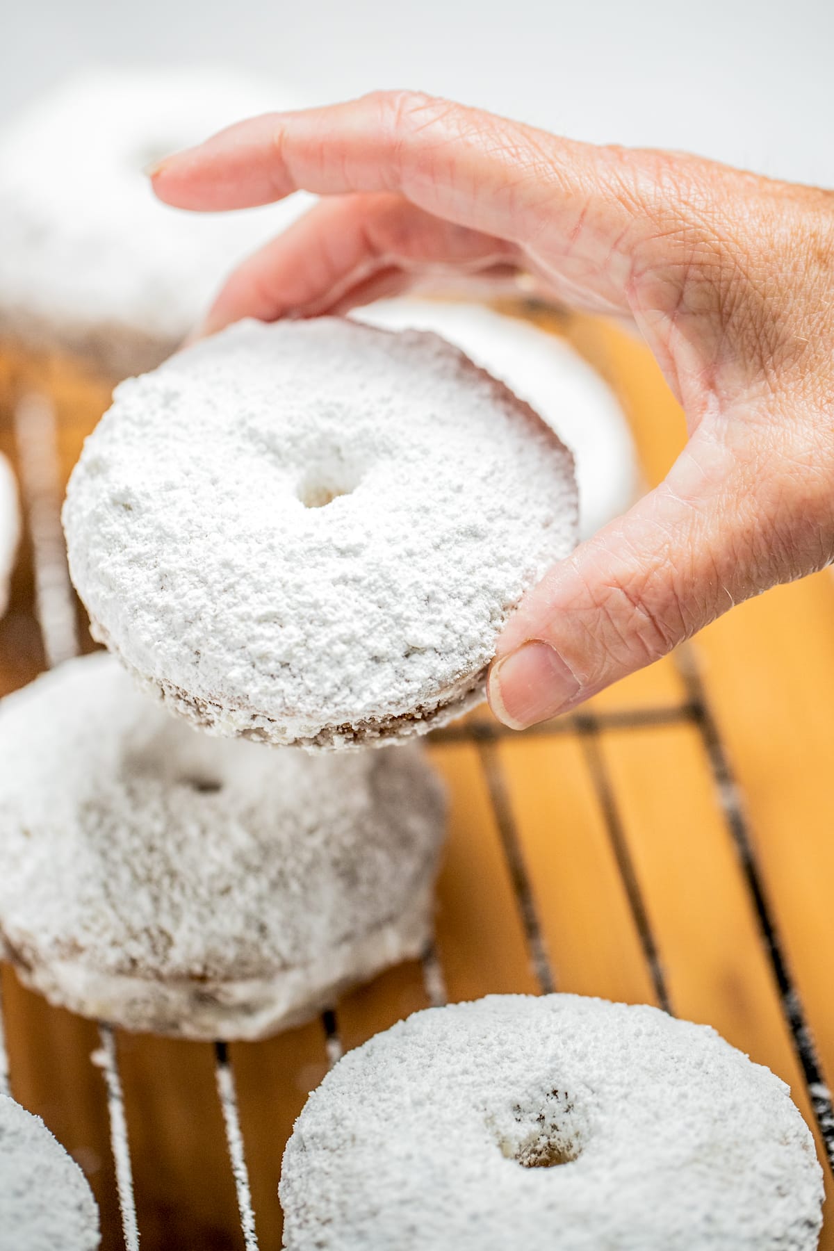 A hand holding a powdered sugar donut over a cooling rack.