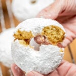 Two hands breaking a powdered sugar donut in half.